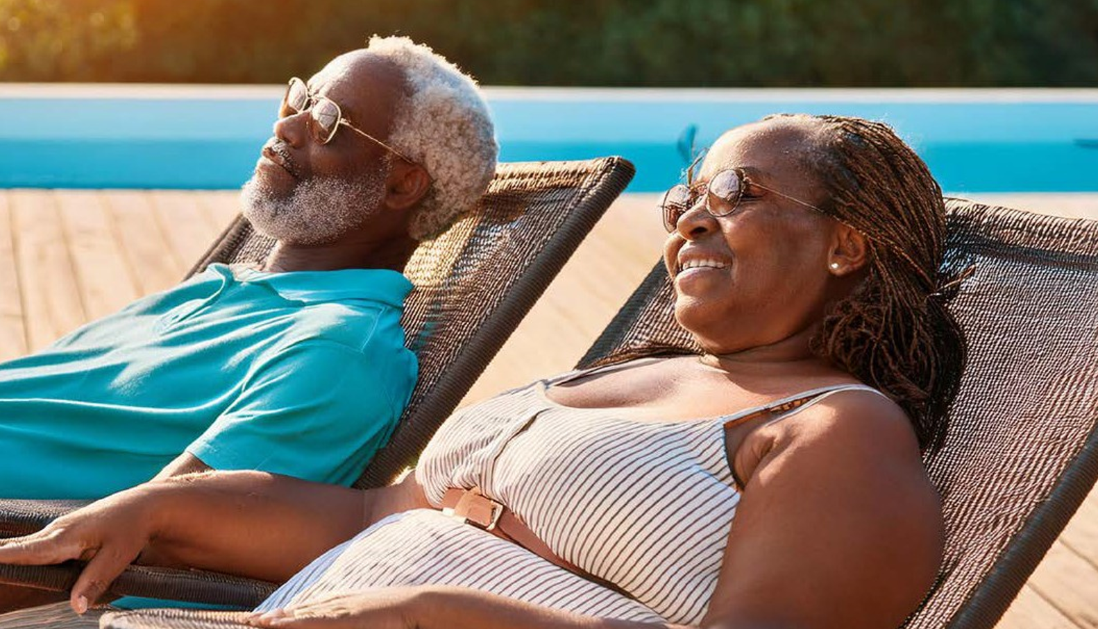 A man and woman in summer attire relax on pool loungers while smiling