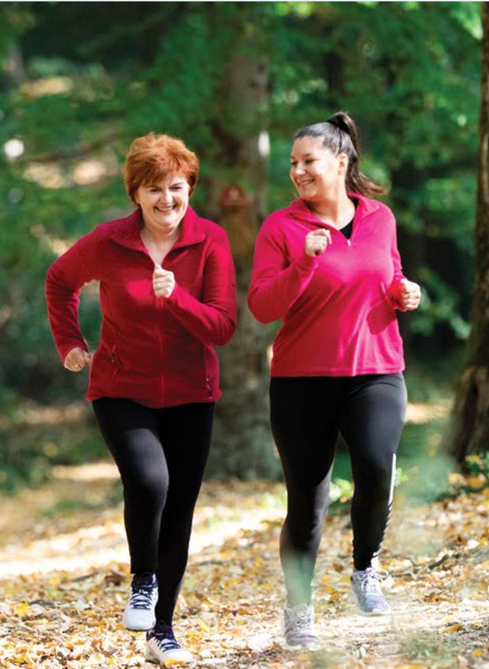 Two smiling women are jogging along a forested trail